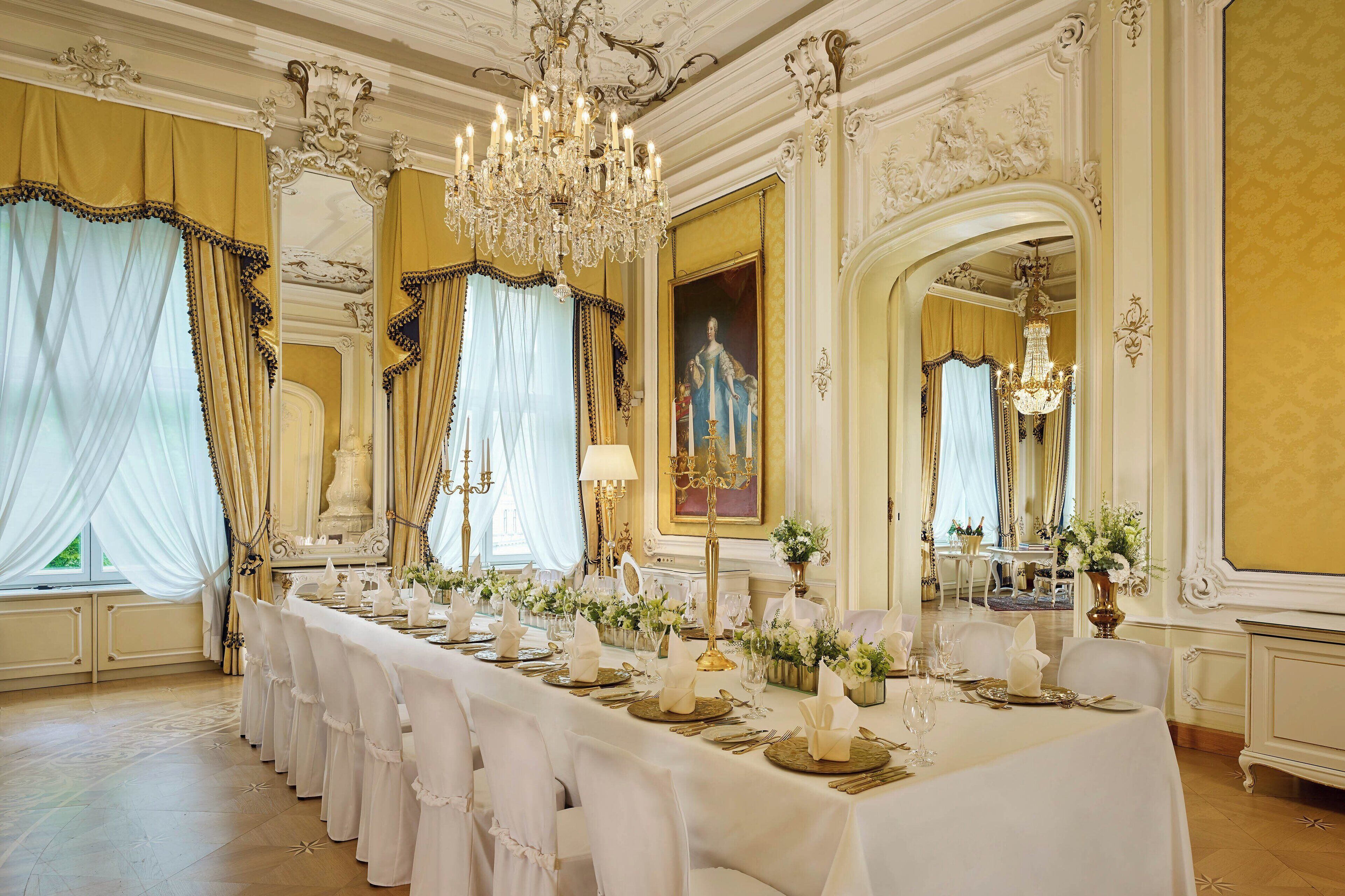 A formal dining room with a long table set for a meal, ornate chandeliers, and classical architecture.