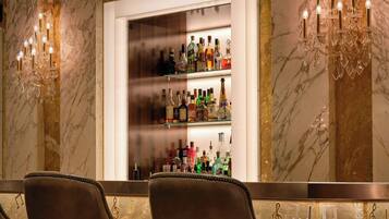Zona de bar con paredes de mármol, una partición de vidrio y una variedad de botellas. Hay tres taburetes con un diseño de nota musical.