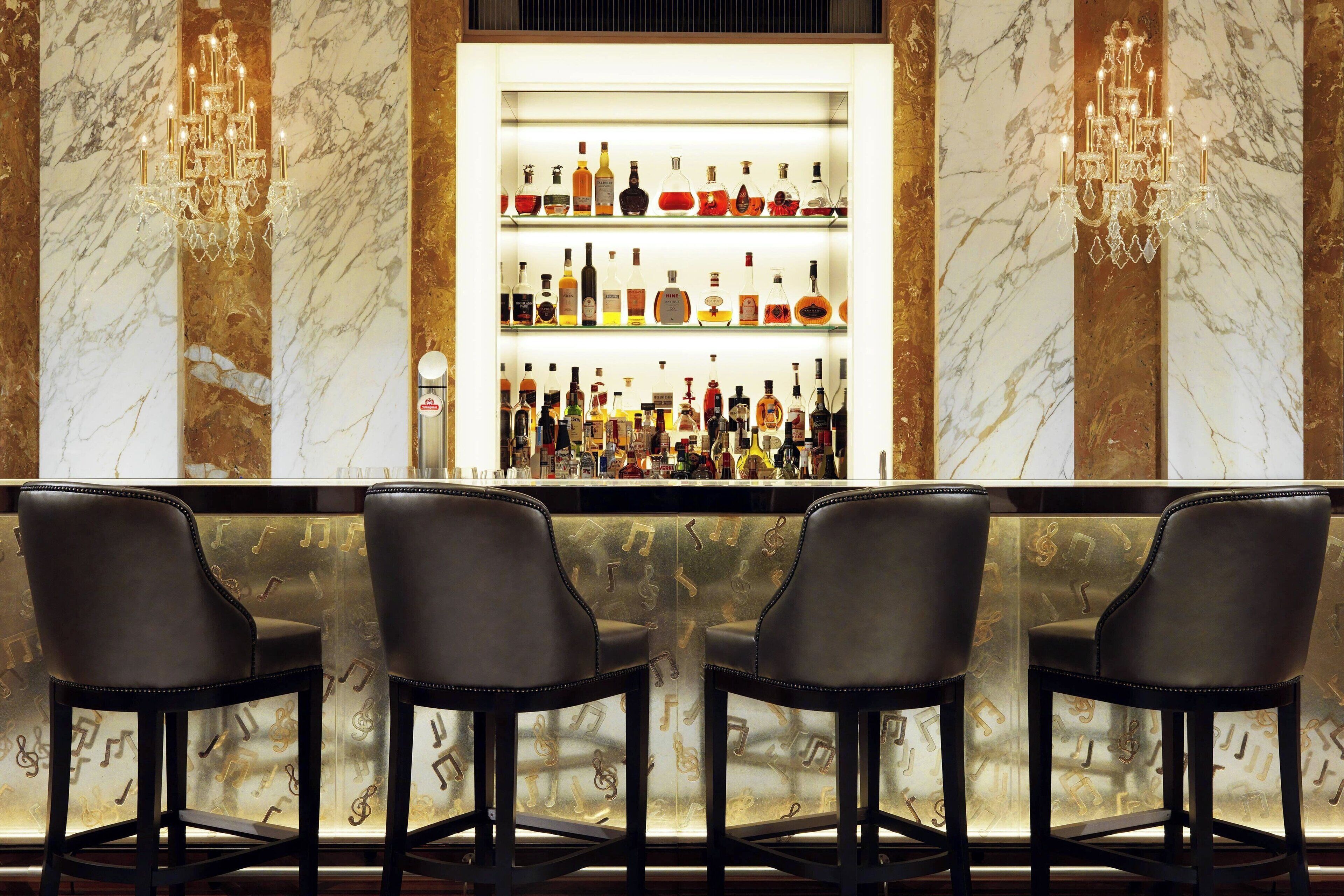 A bar area with three leather chairs, a marble wall, and a shelf of liquor bottles.