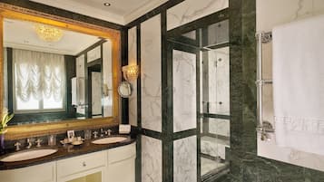 Un baño lujoso con paredes de mármol, un espejo grande, lavamanos dobles y ducha con mampara de vidrio.