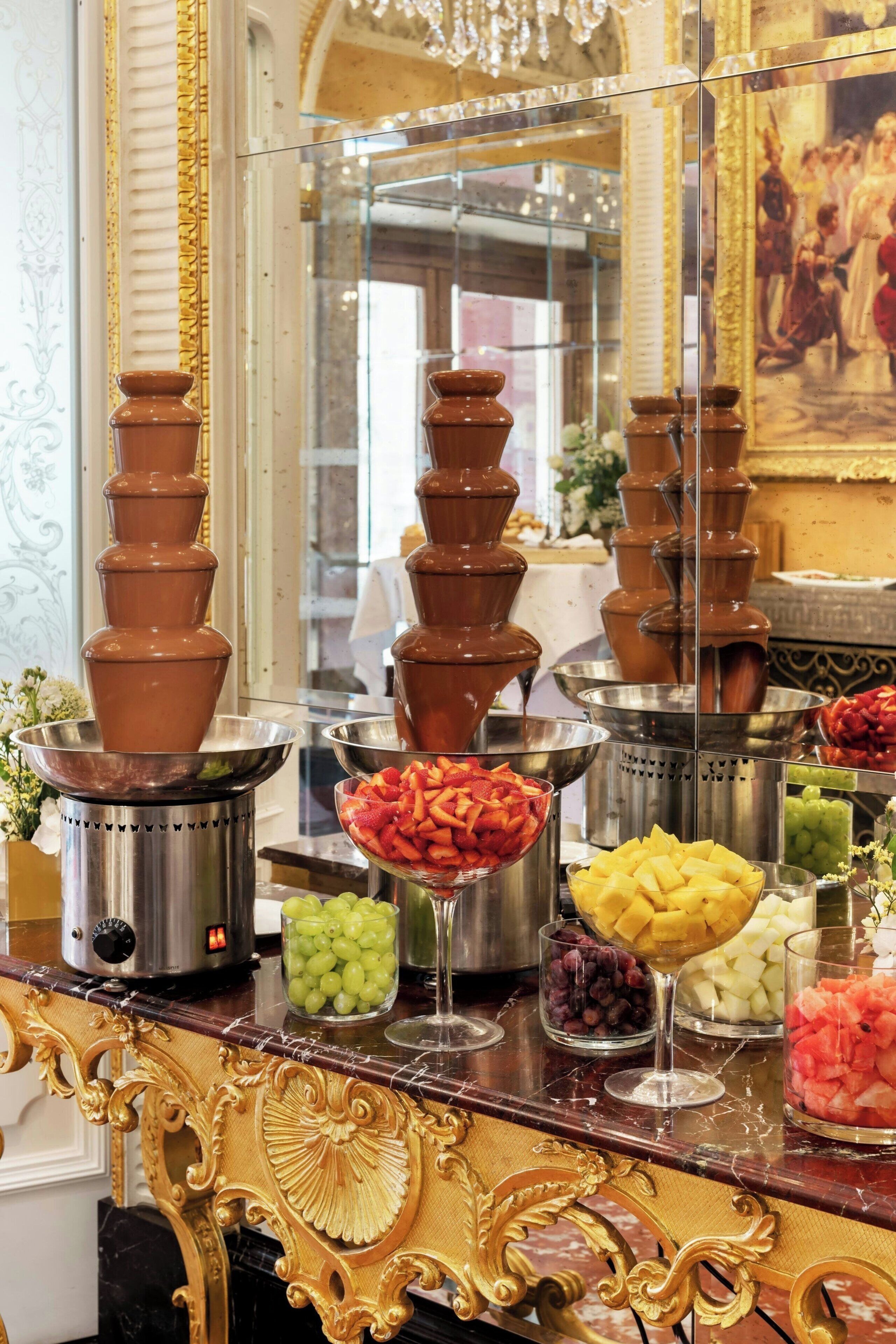 Un bufé con fuentes de chocolate escalonadas y diferentes fuentes de fruta.