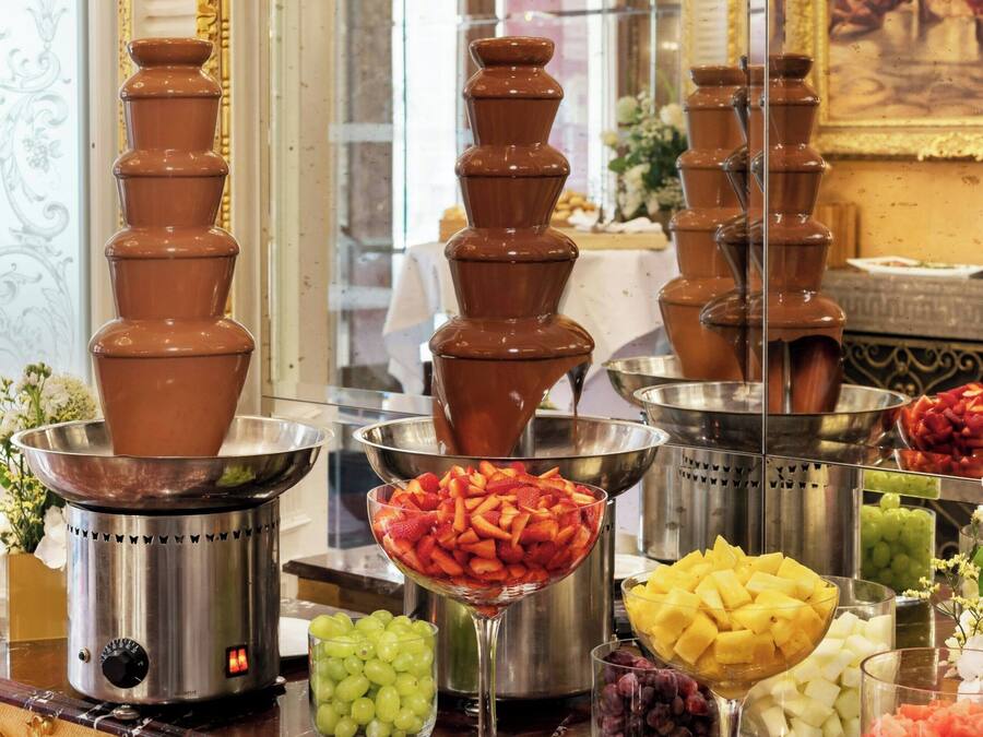 A buffet with tiered chocolate fountains and various fruit bowls.
