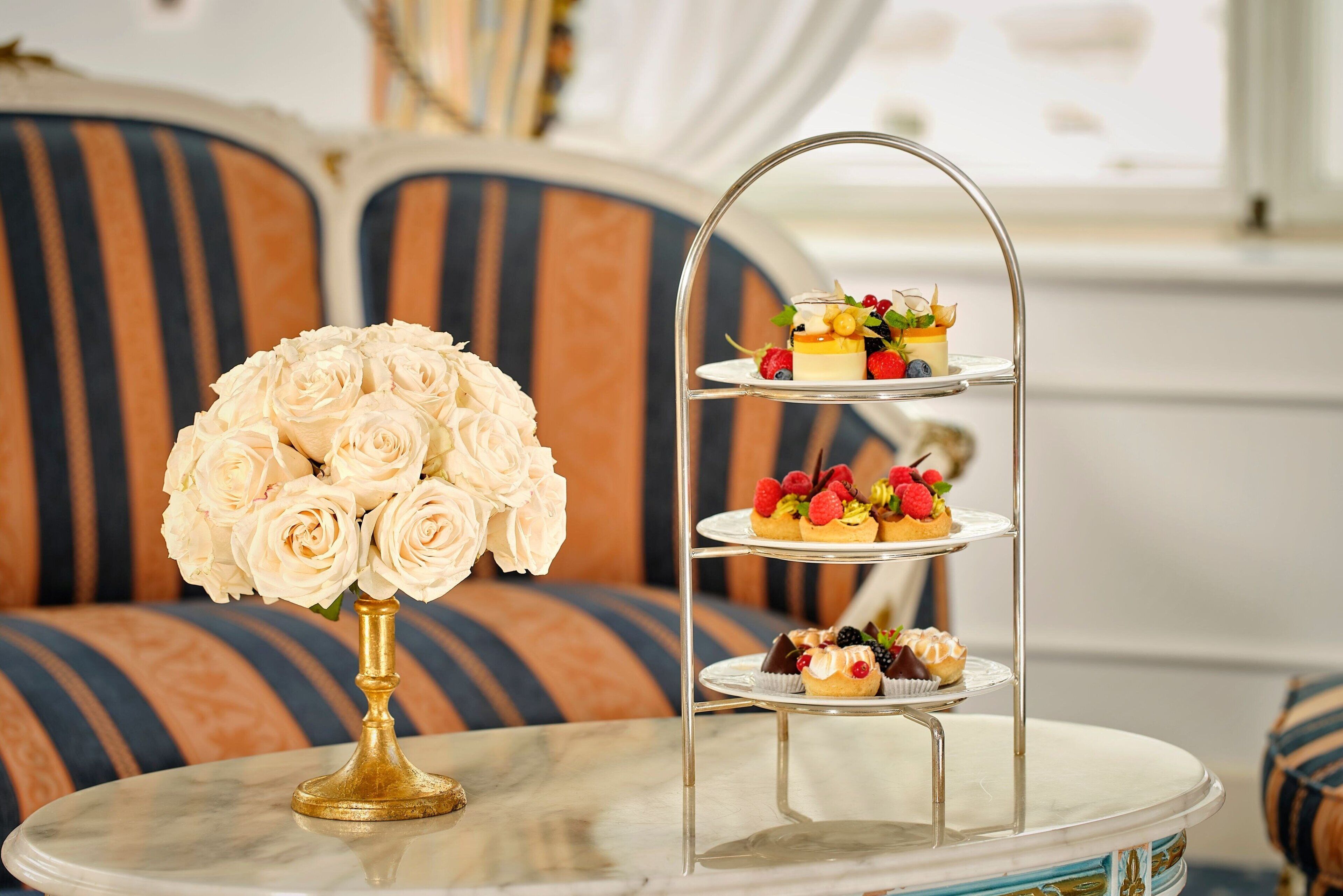 A three-tiered dessert stand with various pastries and a bouquet of white roses on a marble table.