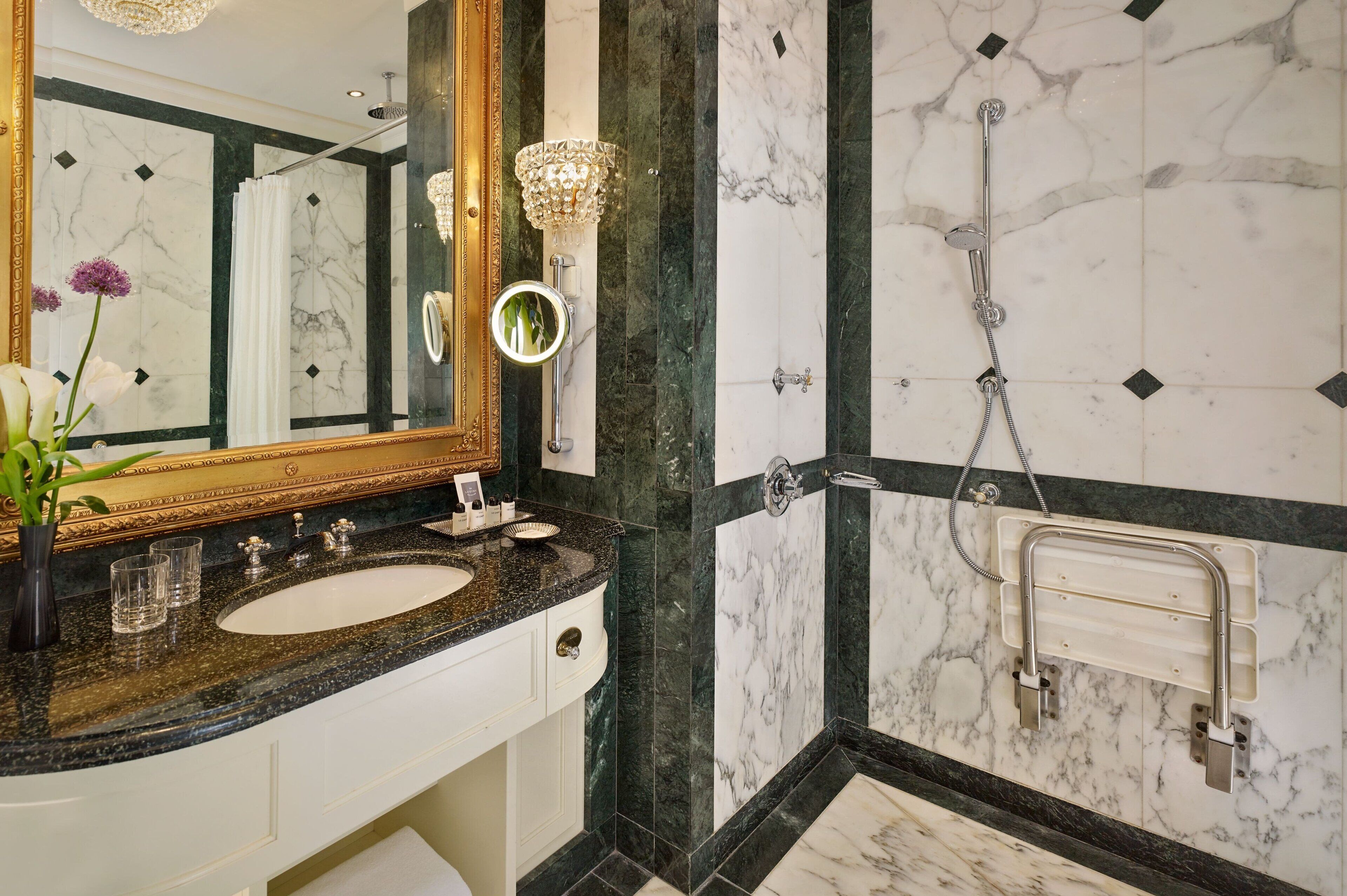 A bathroom with a marble sink, a large mirror, a shower with a handheld showerhead, and a towel rack.
