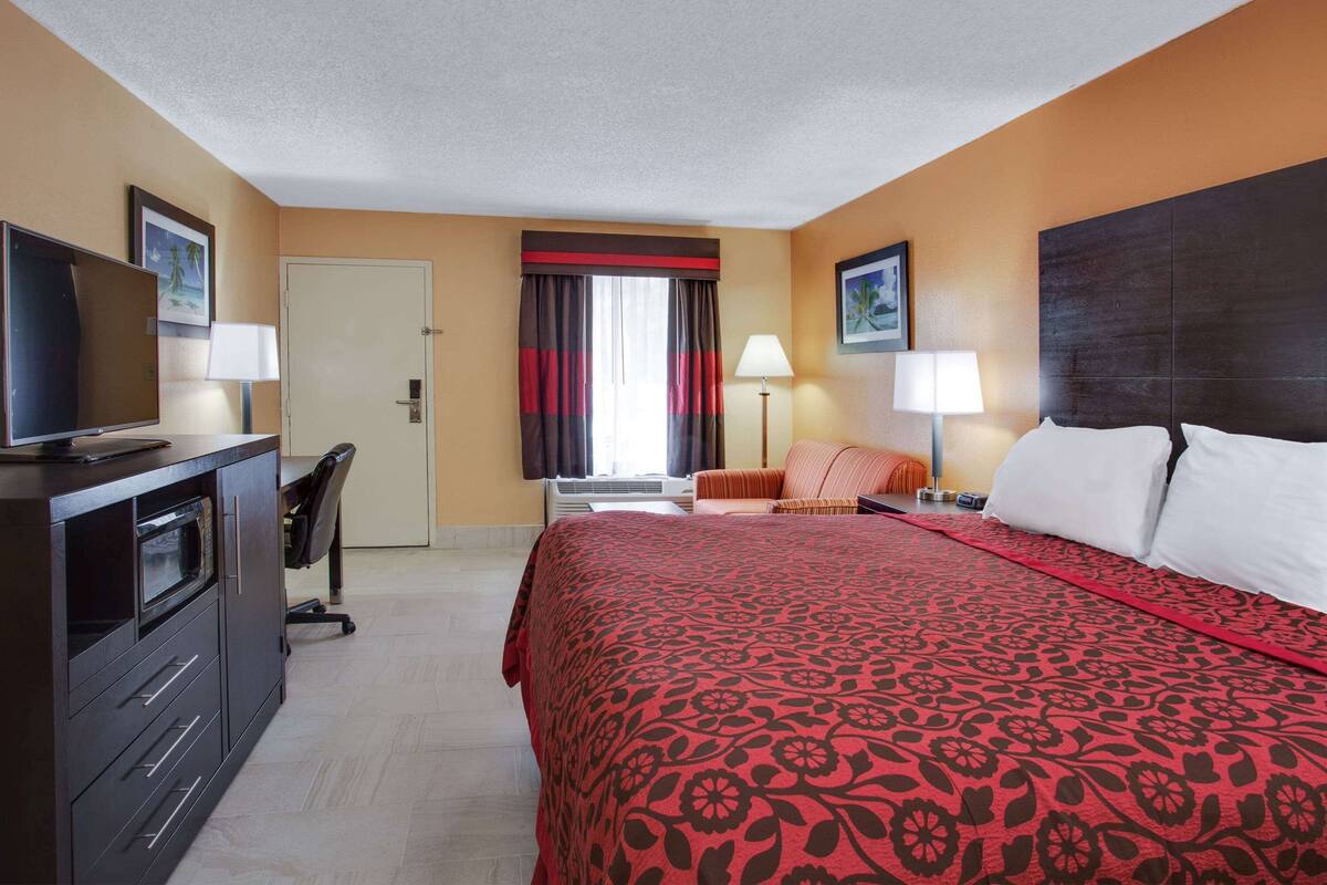 Une chambre d’hôtel avec un lit, un bureau avec un ordinateur, une télévision et une chaise.