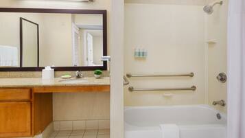 A bathroom with a sink, mirror, and a shower area with grab bars.
