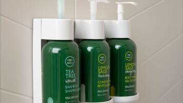 Three bottles of tea tree shampoo and two bottles of lemon sage body wash on a shelf.