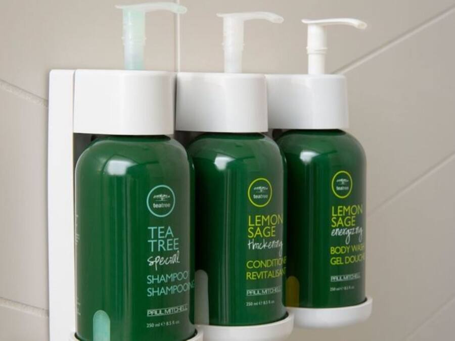 Three bottles of tea tree shampoo and two bottles of lemon sage body wash on a shelf.