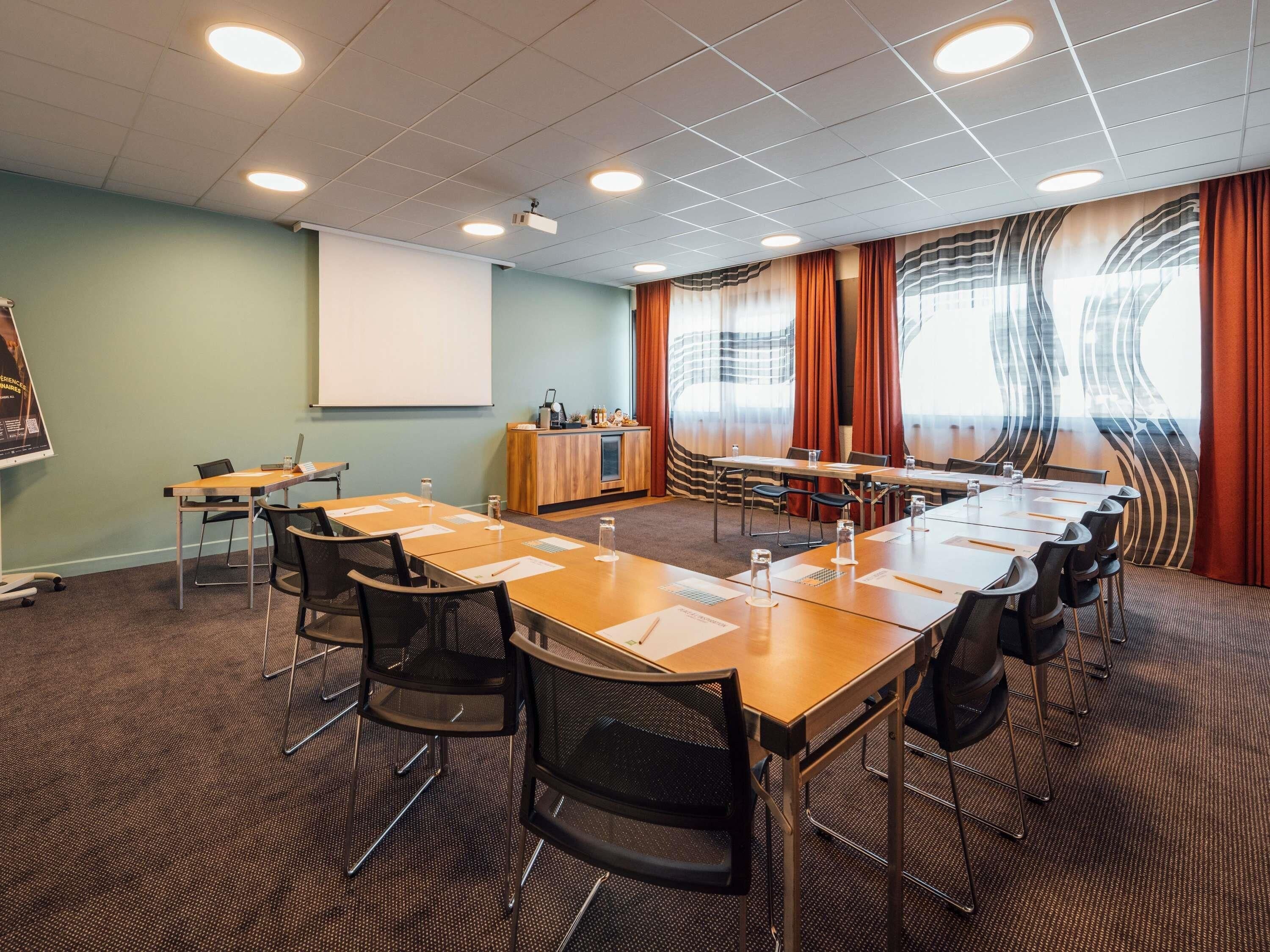 Un salón de conferencias con una larga mesa, sillas, una pantalla de proyector y un atril.