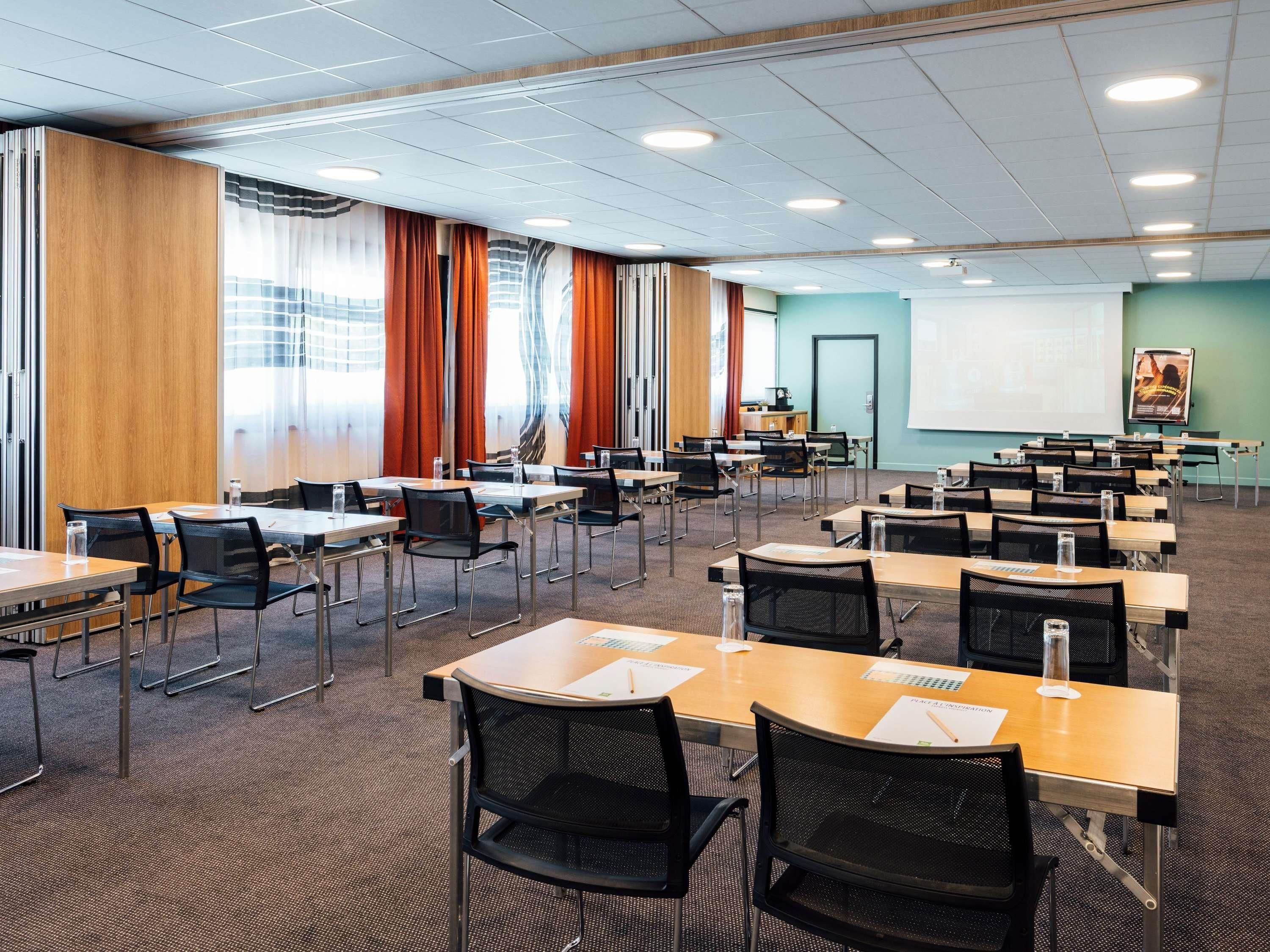 A conference room with multiple tables and chairs, a projector screen, and a presentation board.