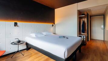 A modern hotel room with a large bed, a bedside table with a lamp, a wardrobe, and a shower area.