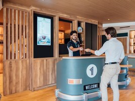 Un mostrador de recepción con un cartel que dice 'WELCOME', una pantalla digital con el menú y un interior de madera.