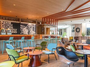 A modern bar area with a wooden ceiling, a 'Please Do Not Disturb' sign, and a variety of seating options including round tables and colorful chairs. - ibis Styles Lyon Sud Vienne (Chasse-sur-Rhone)