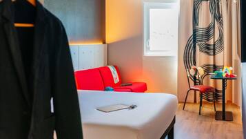A hotel room with a bed, a red sofa, a small table with toys, and a window with curtains.