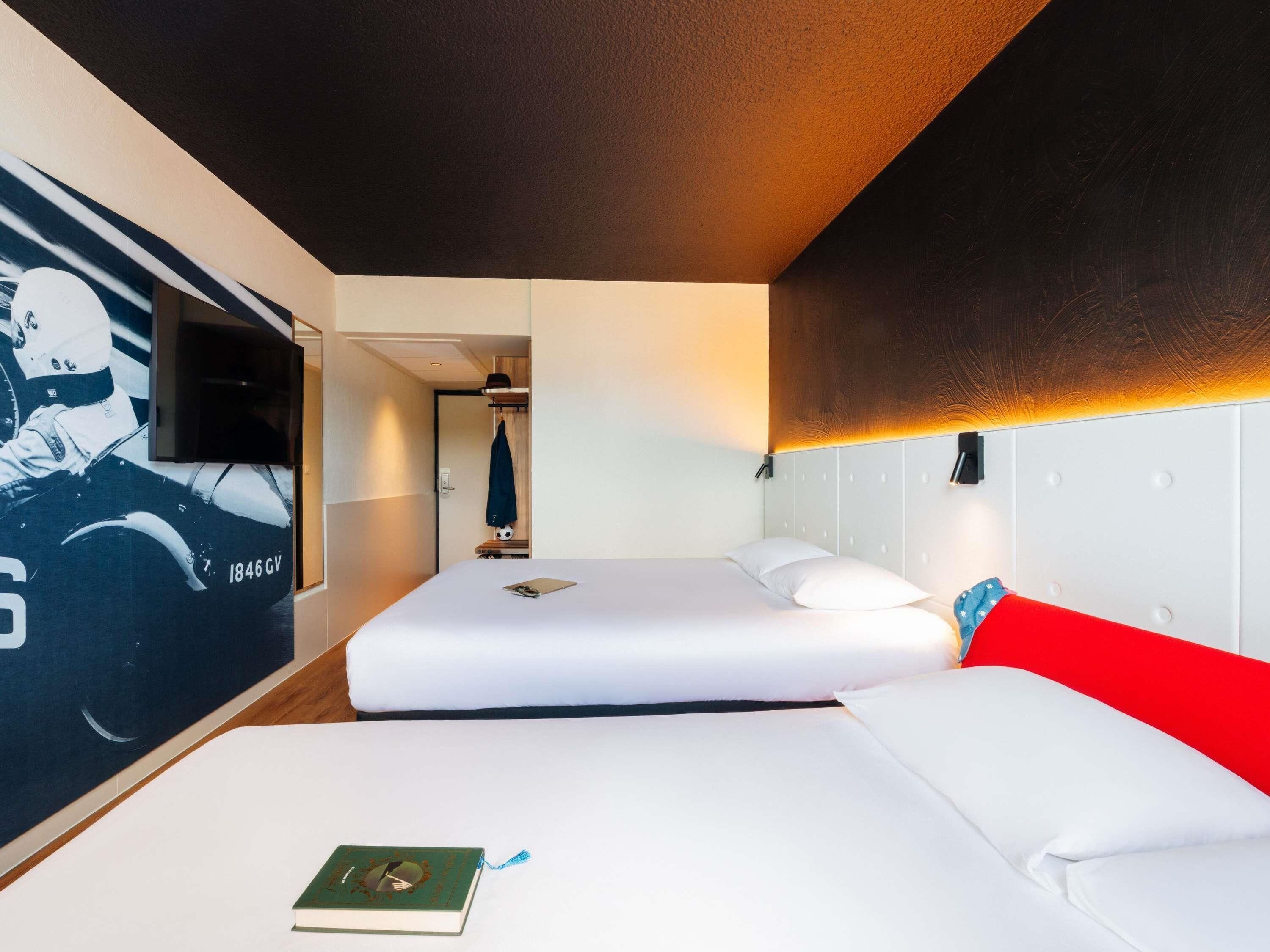 Habitación de hotel con dos camas, un televisor montado en la pared y una puerta que da a un baño.