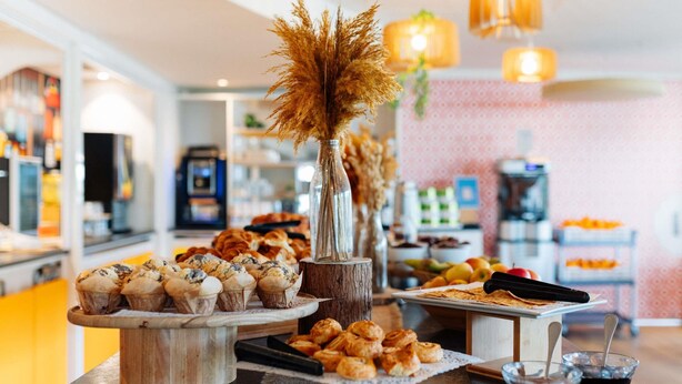 A buffet table with various pastries, a vase with dried flowers, and condiments. - ibis Styles Lyon Sud Vienne (Chasse-sur-Rhone)