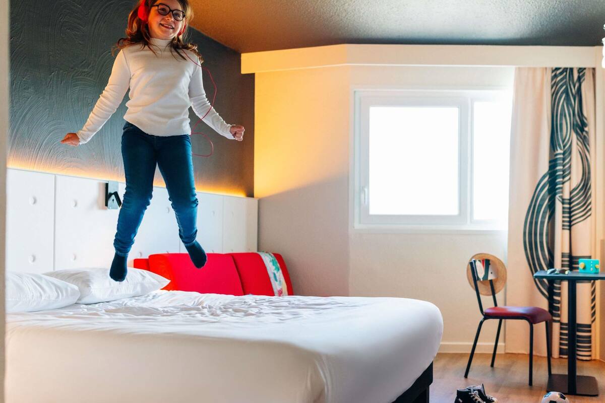 A room with a bed, a window, a chair, and a table with a soccer ball.