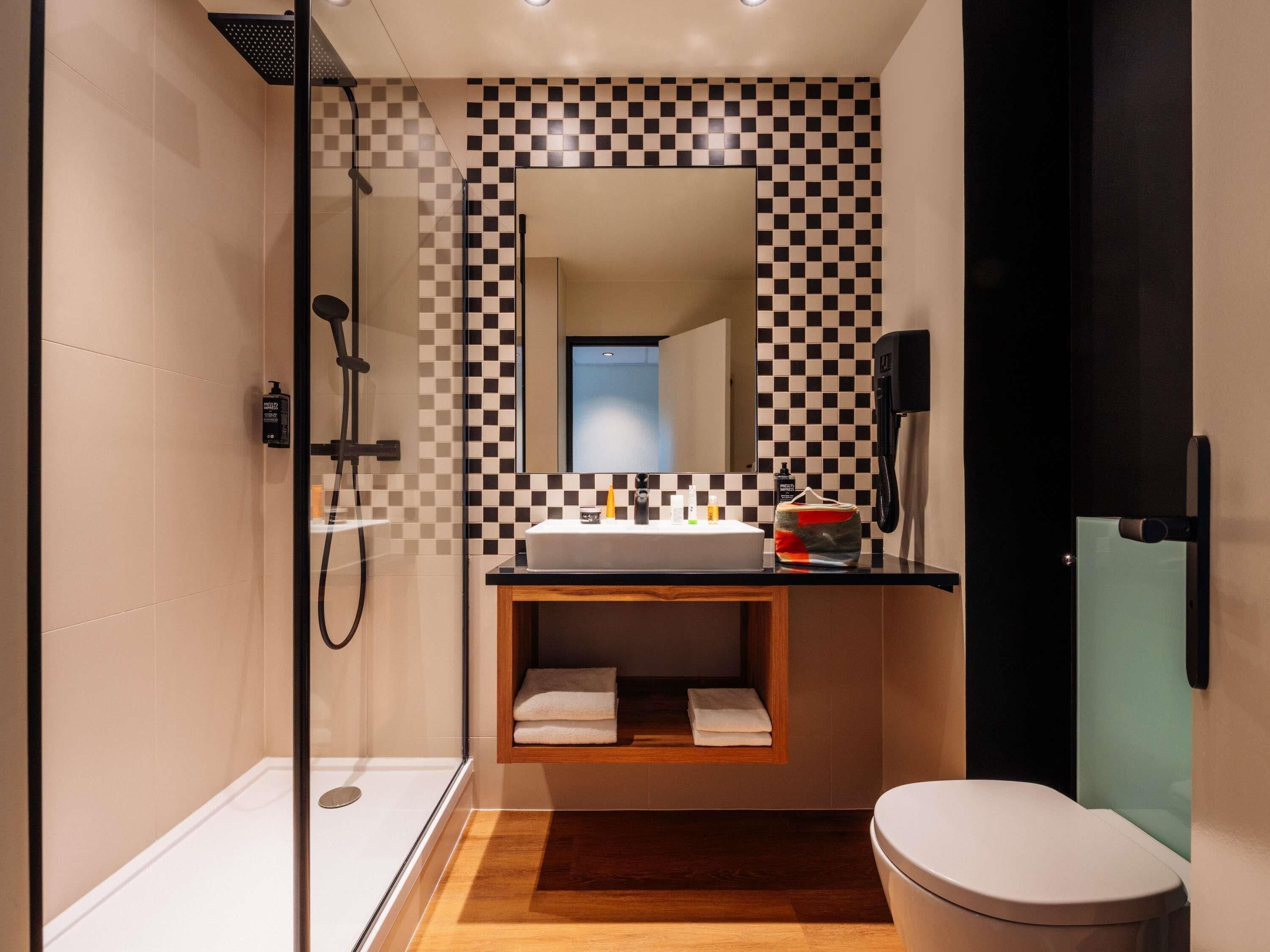 A modern bathroom with a checkered wall pattern, a white sink, a glass shower enclosure, and a toilet.