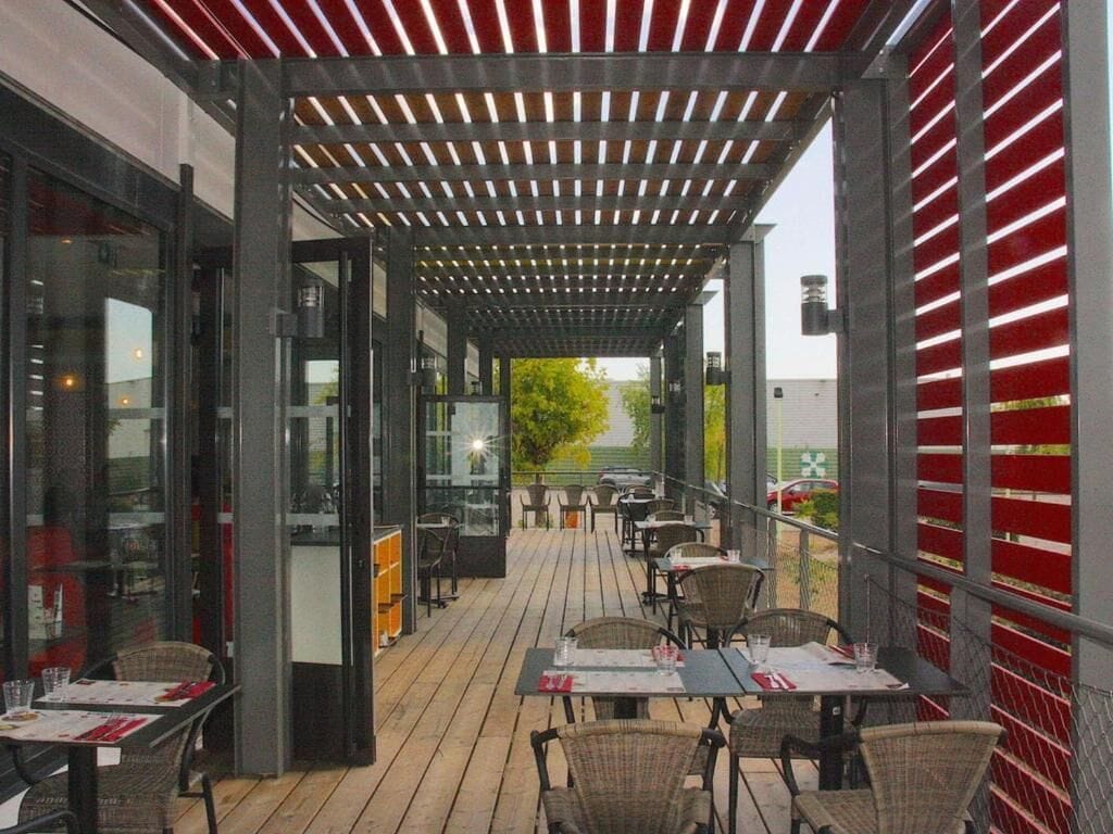 Une terrasse extérieure avec des tables et des chaises, un espace salon couvert et une vue sur la rue.