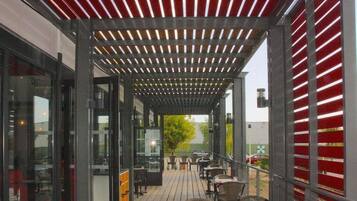 Une terrasse extérieure avec des tables et des chaises, un espace salon couvert et une vue sur la rue.