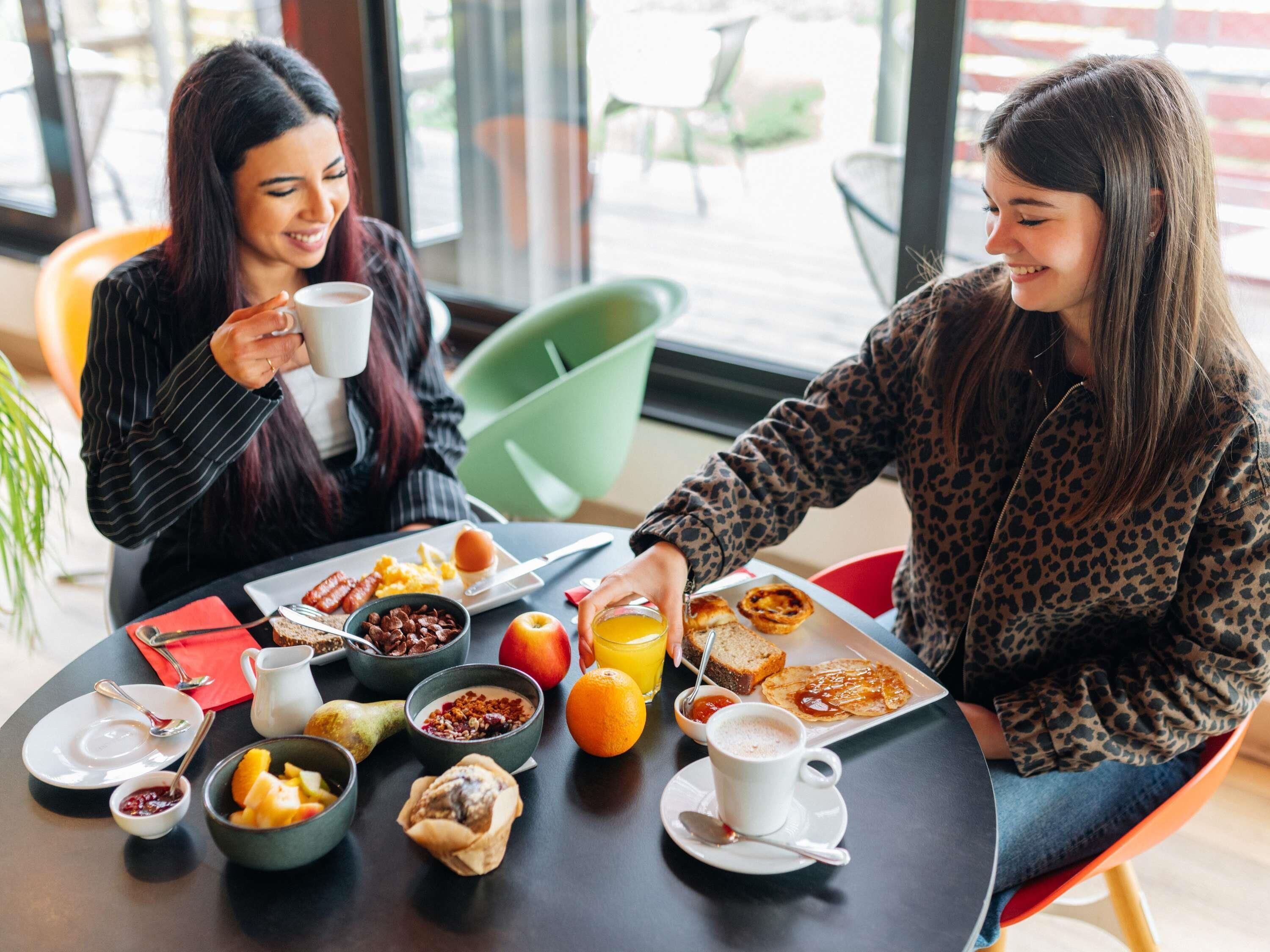 Dos personas sentadas a una mesa con alimentos para el desayuno, como huevos, tostadas y fruta.