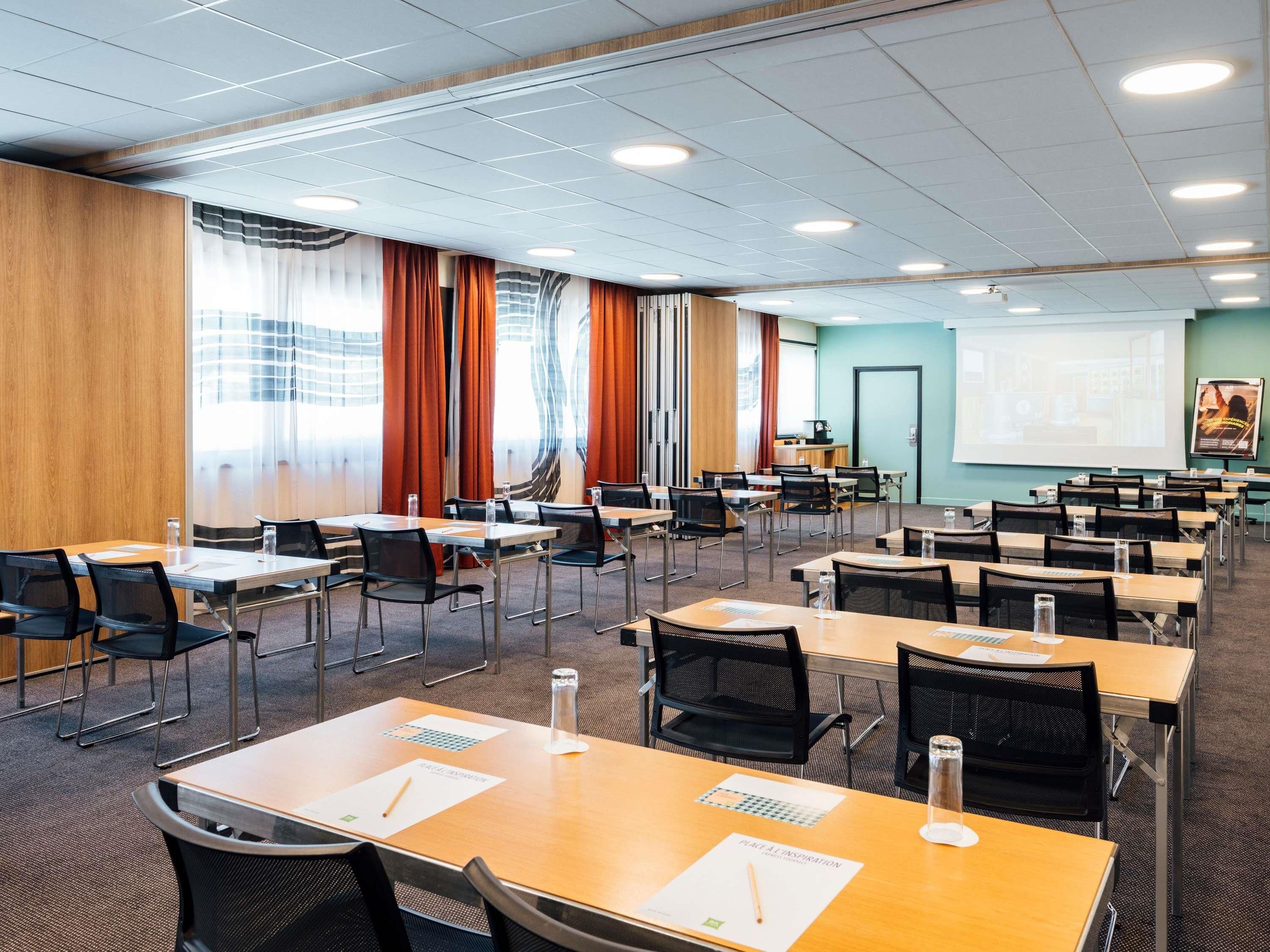 A conference room with multiple tables and chairs, a projector screen, and a presentation area.