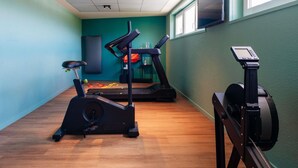 A gym with exercise equipment, a wall-mounted TV, and a window. - ibis Styles Lyon Sud Vienne (Chasse-sur-Rhone)