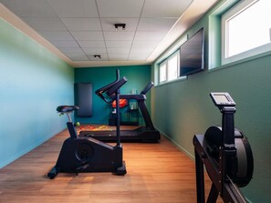 A gym with exercise equipment, a wall-mounted TV, and a window. - ibis Styles Lyon Sud Vienne (Chasse-sur-Rhone)