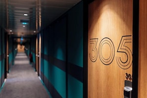 A hallway with a wooden door labeled '305' and a carpeted floor. - ibis Styles Lyon Sud Vienne (Chasse-sur-Rhone)