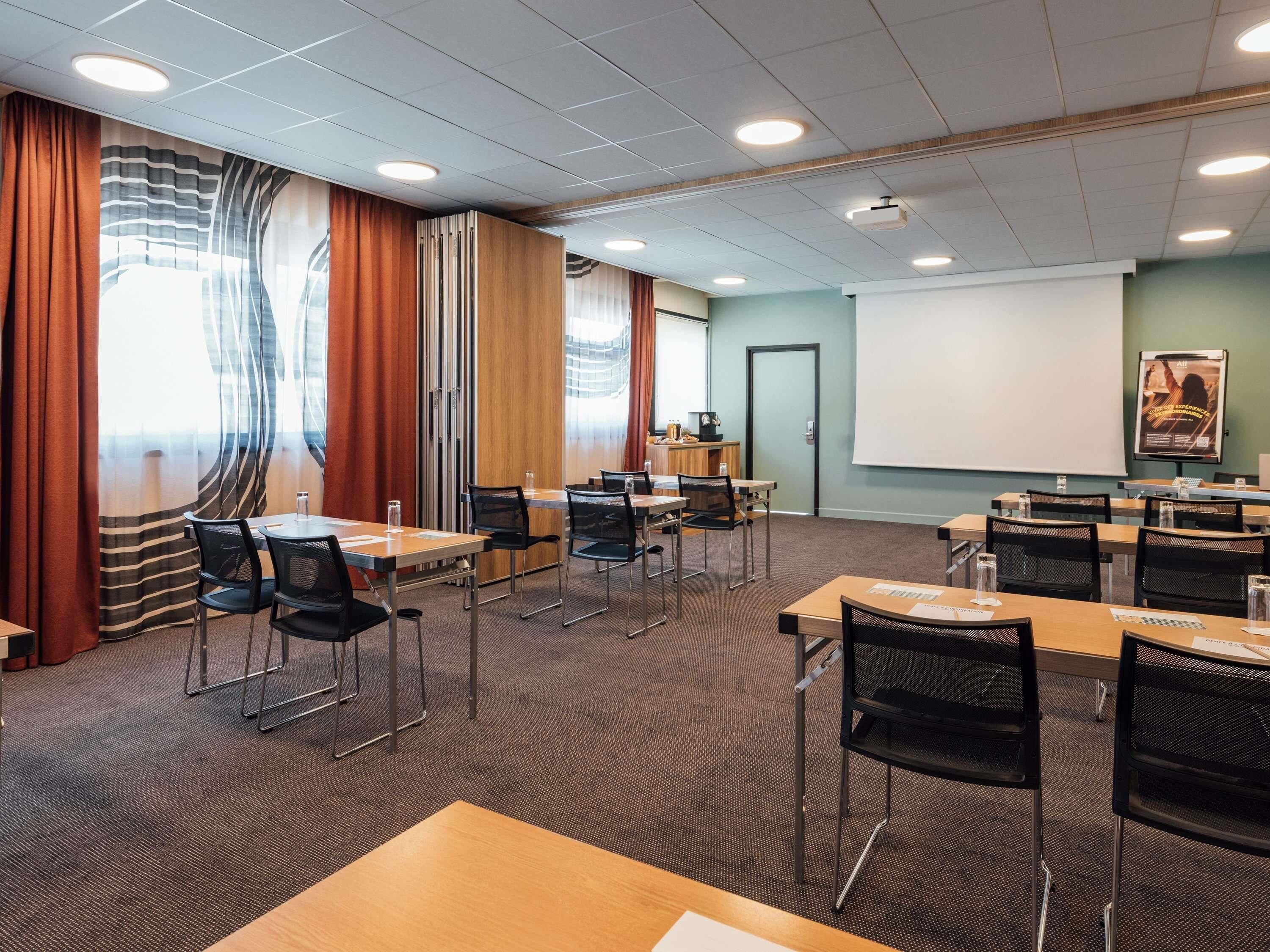 Een vergaderruimte met tafels, stoelen, een projectiescherm en een presentatiebord.