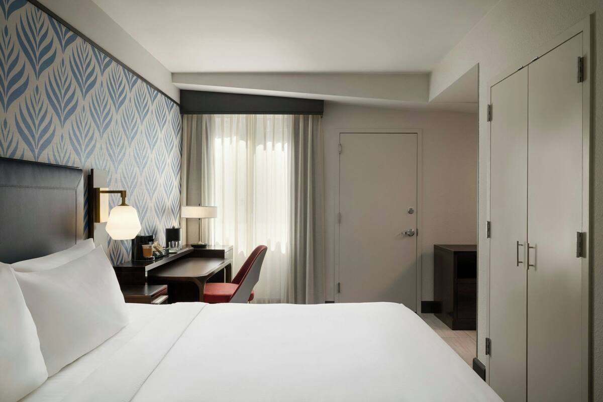 Una habitación de hotel con cama, escritorio, silla y armario.