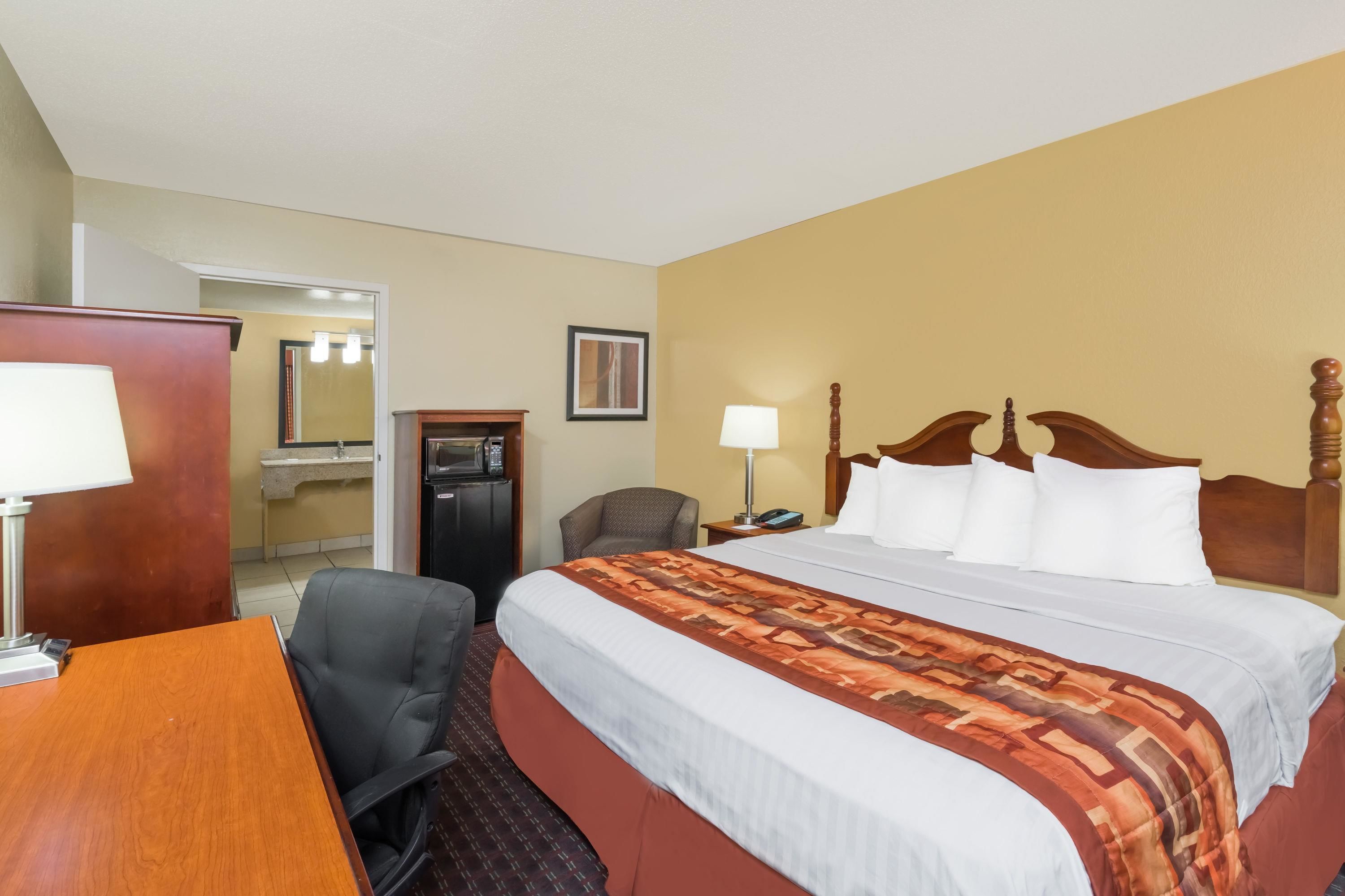 A hotel room with a large bed, a desk with a lamp, a chair, a desk lamp, a telephone, and a mirror.