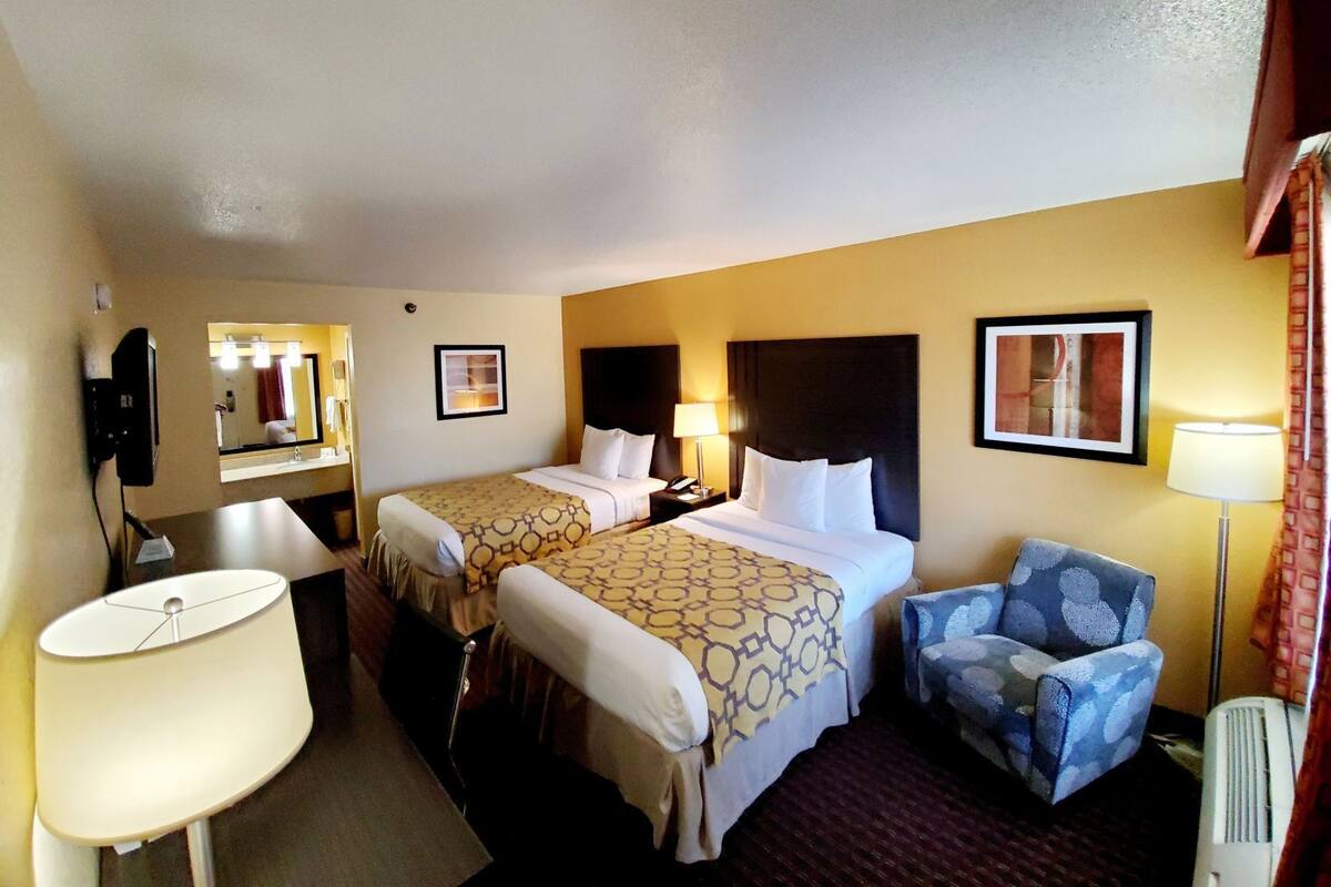 Une chambre d’hôtel avec deux lits, un bureau, une chaise, un miroir et une lampe.