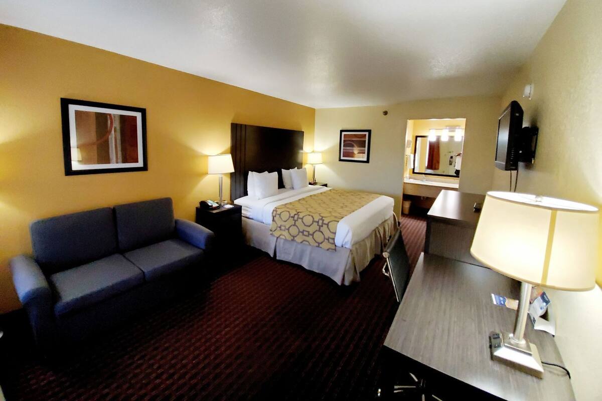Une chambre d’hôtel comprenant un lit, un bureau, une chaise, un canapé et deux tables de chevet avec des lampes.