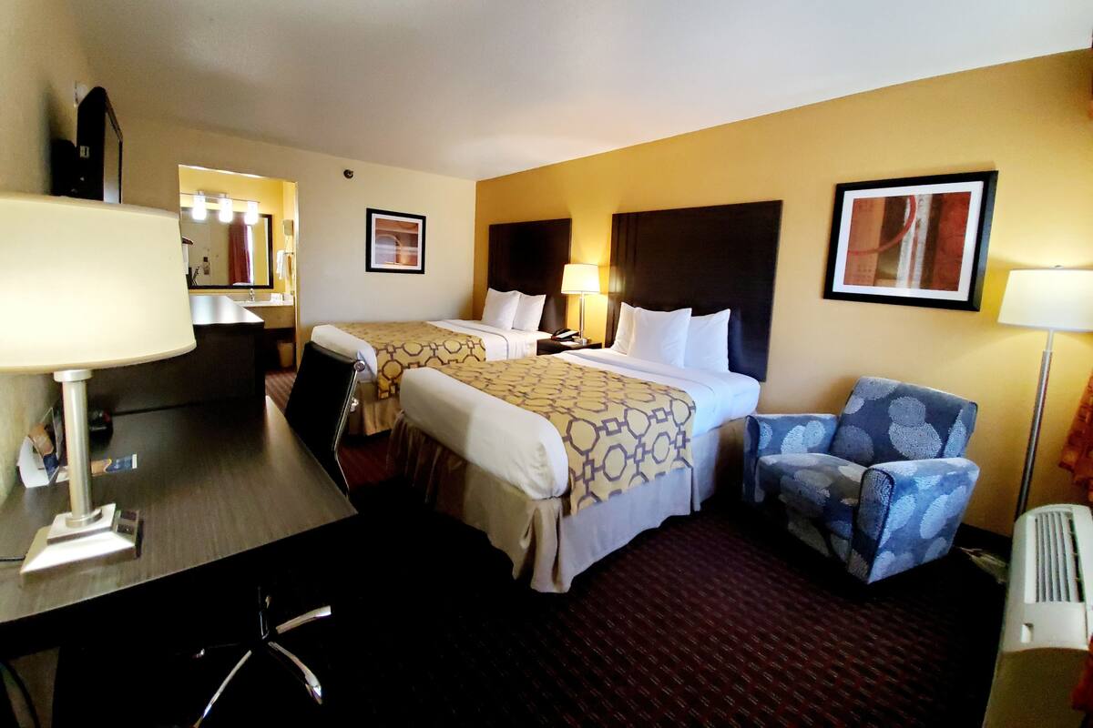 Une chambre d’hôtel avec deux lits, un bureau, une chaise, une lampe et un tableau au mur.