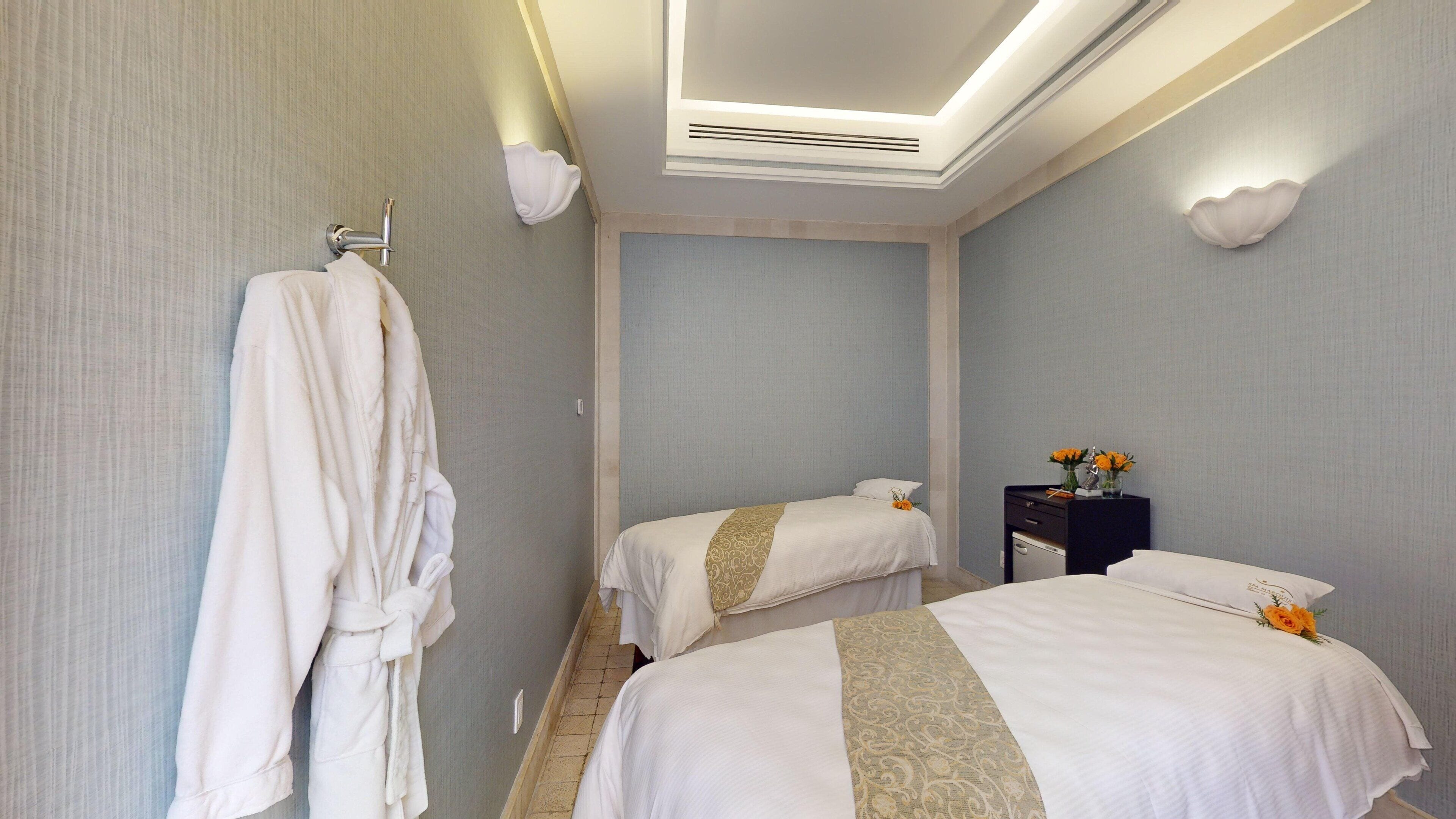 Quarto de hotel com duas camas, um roupão pendurado na parede e uma pequena mesa com flores.