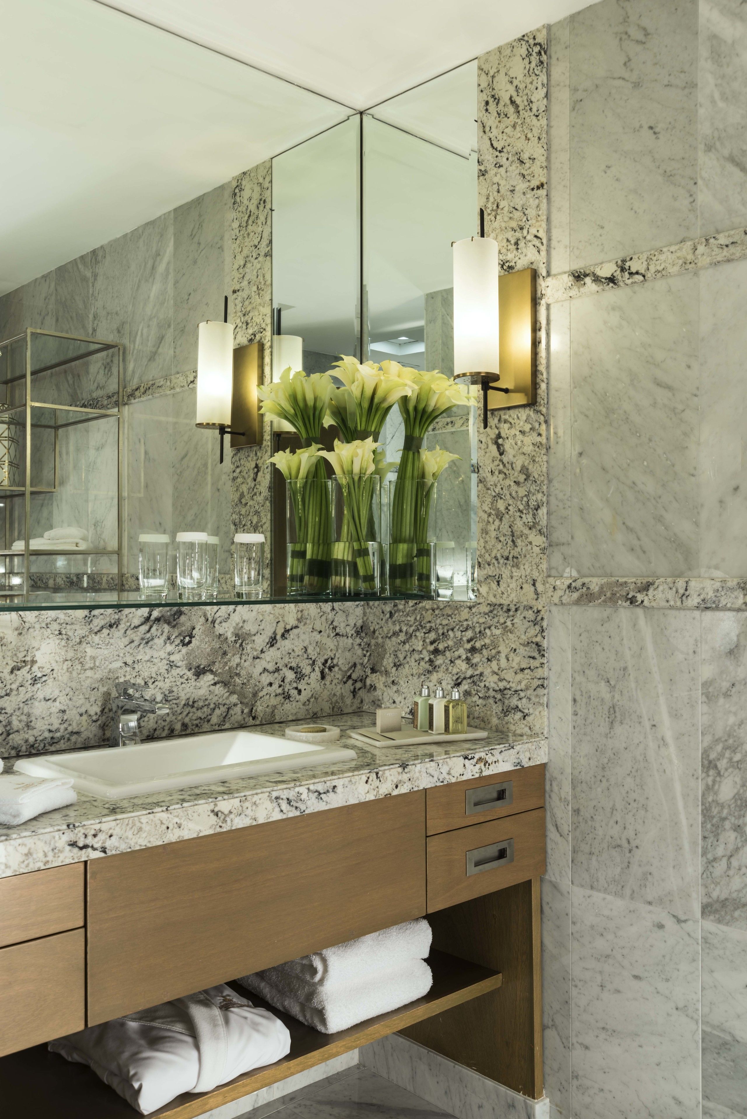 A modern bathroom with a marble sink, a large mirror, and a vase of flowers.