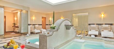 Un área de spa con dos jacuzzis, un frutero, toallas y una copa de vino sobre una mesa.