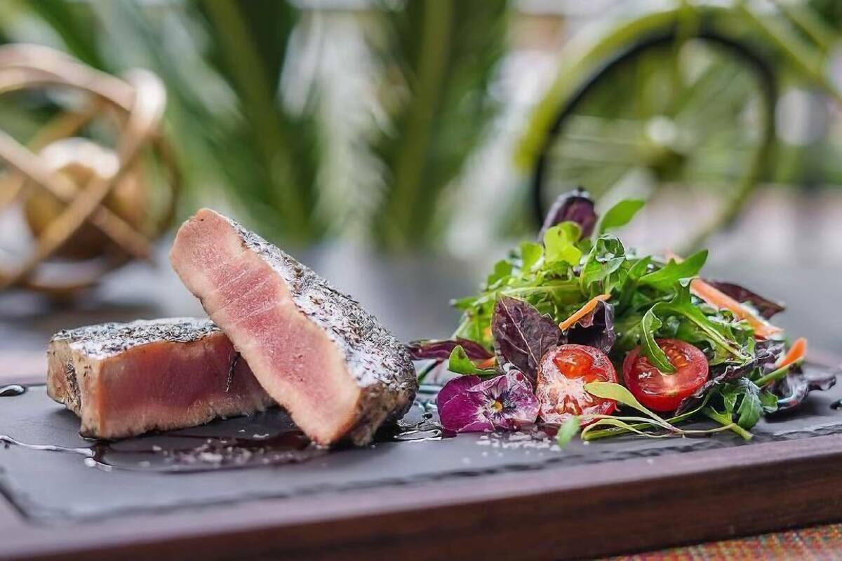 A steak with a dark crust on a slate plate, accompanied by a fresh salad with mixed greens and cherry tomatoes.