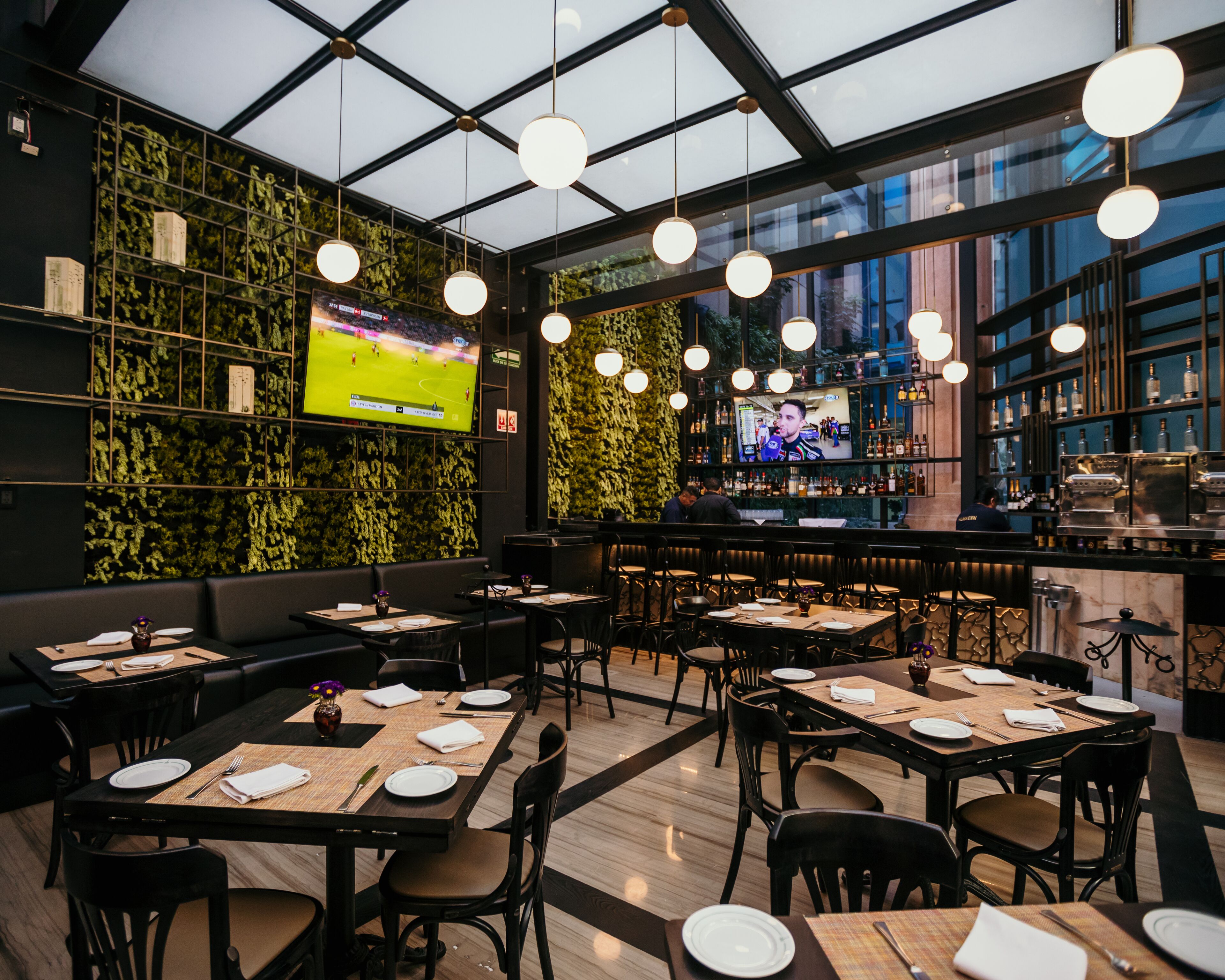 A modern restaurant with a bar area, multiple seating options including tables and booths, and a large TV screen displaying sports.
