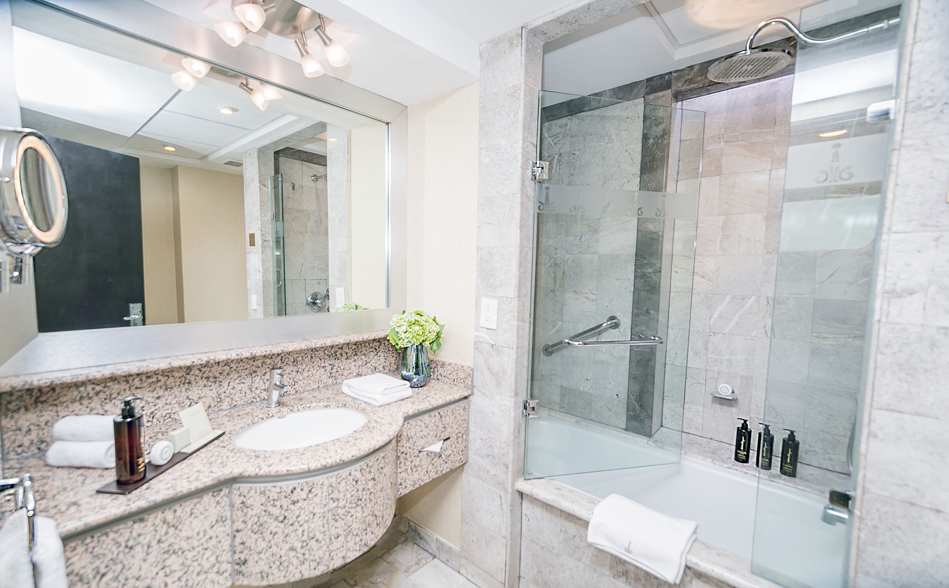 Un baño moderno con encimeras de granito, un espejo grande, ducha con mampara de vidrio y bañera.