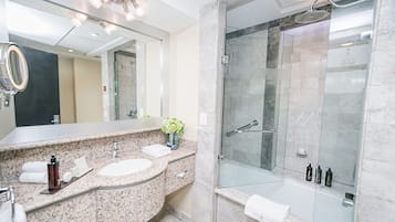 Un baño moderno con encimeras de granito, un espejo grande, ducha con mampara de vidrio y bañera.