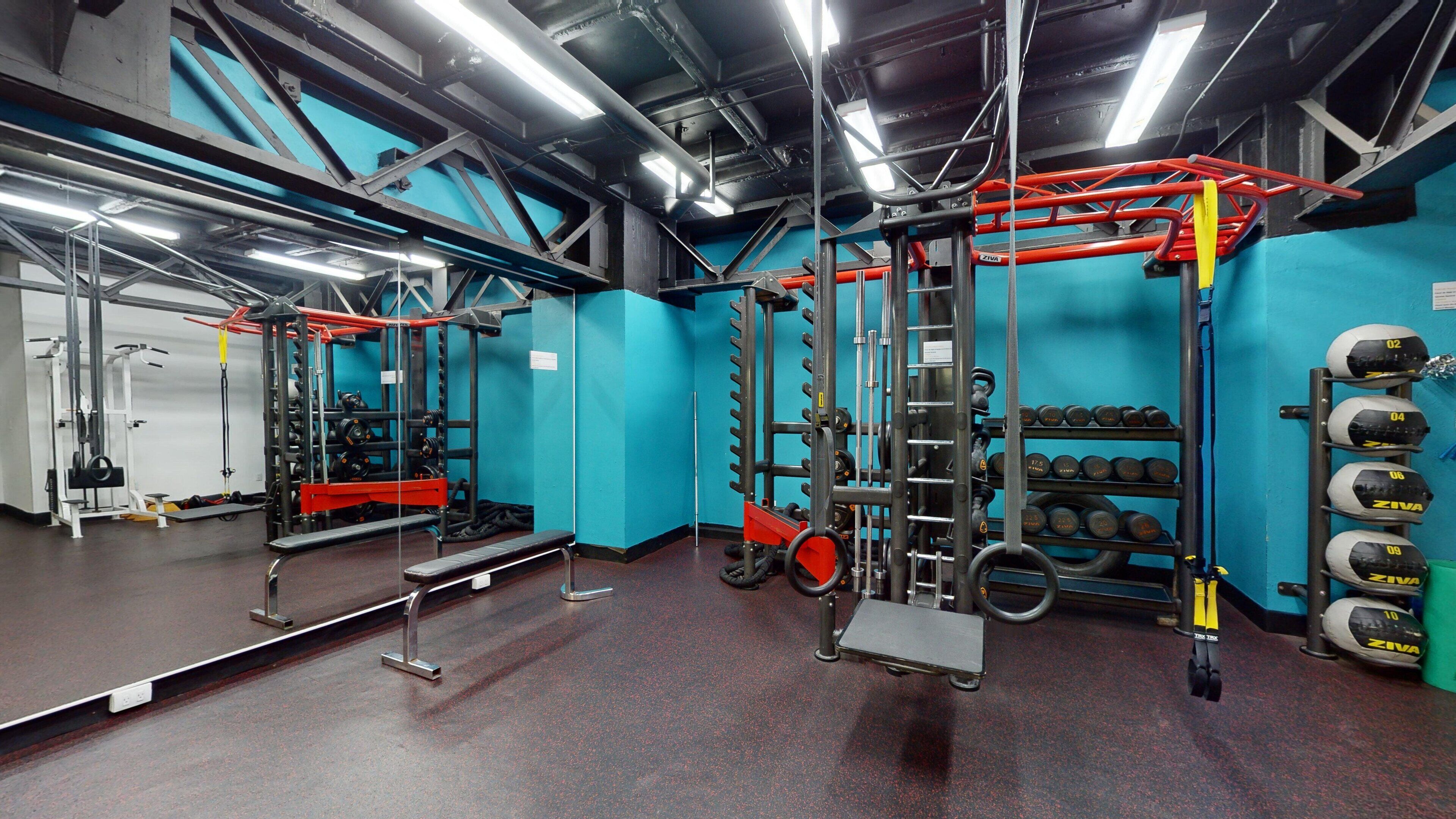 Un gimnasio con equipo de levantamiento de pesas, un espejo y un estante con mancuernas.