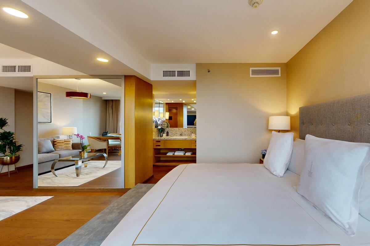 A hotel room with a large bed, a sitting area with a sofa and a coffee table, and a view into the dining area.