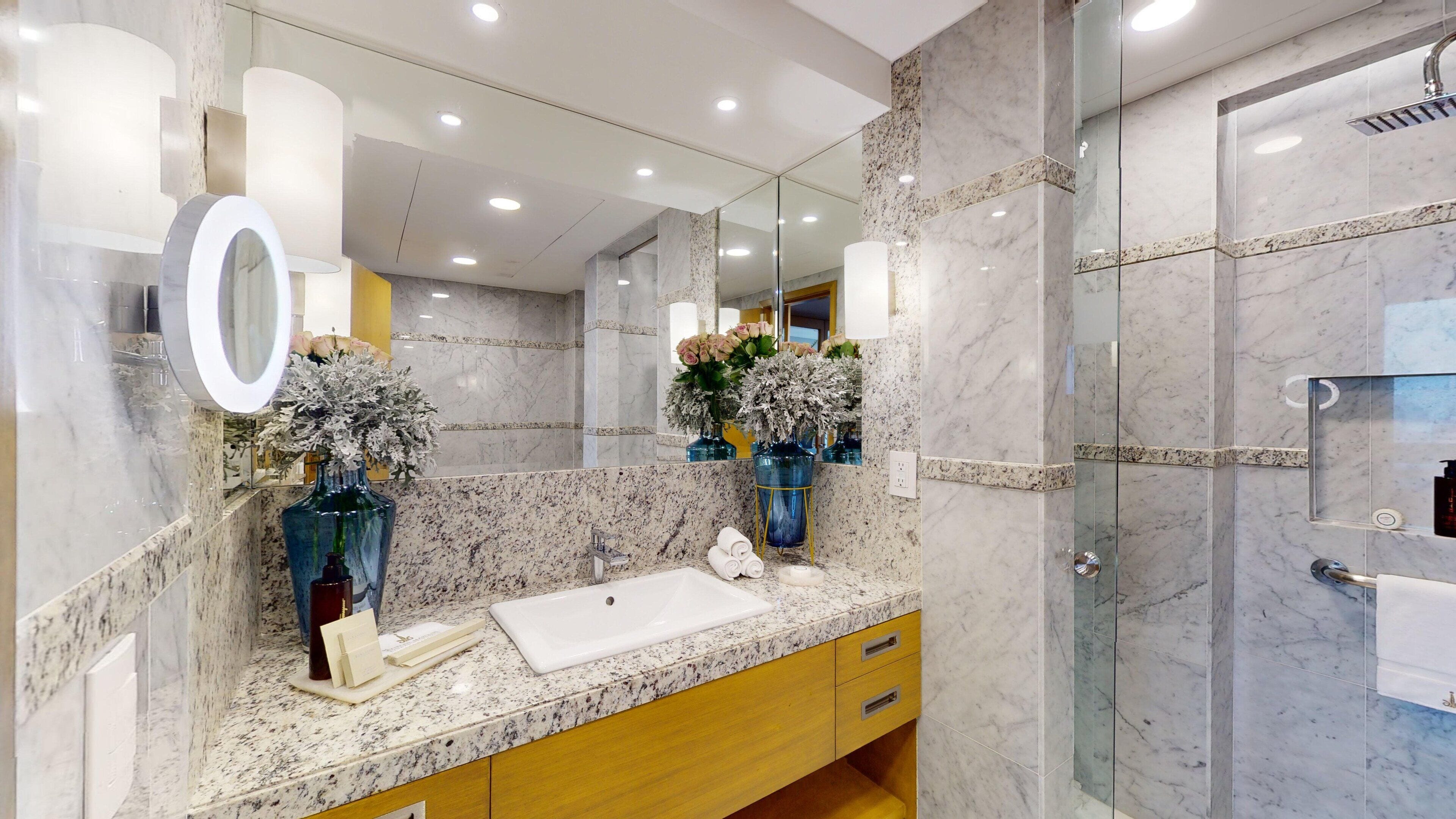 Un baño moderno con encimera de mármol, un espejo grande y cabina de ducha de cristal.