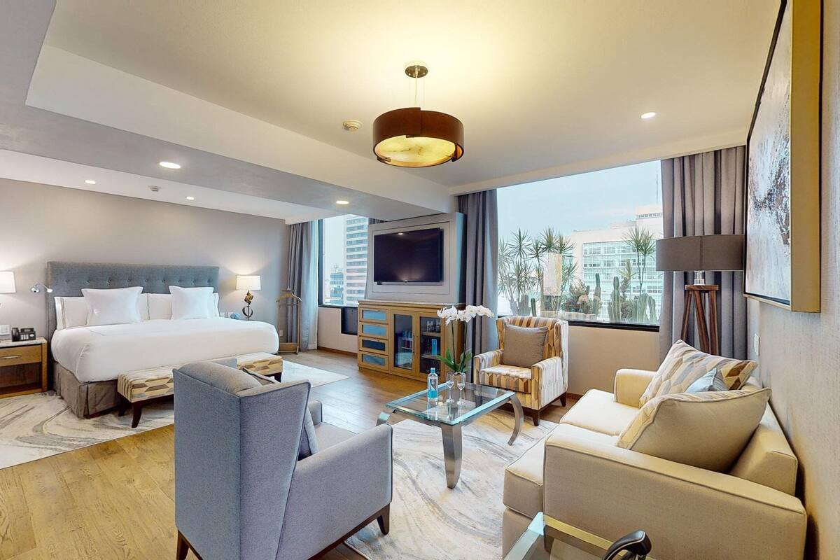 A modern hotel room with a large bed, a TV, a sofa, and a coffee table.