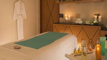 Un cuarto de spa con una cama, un perchero, una camilla de masaje y un mostrador con velas y artículos de aseo.