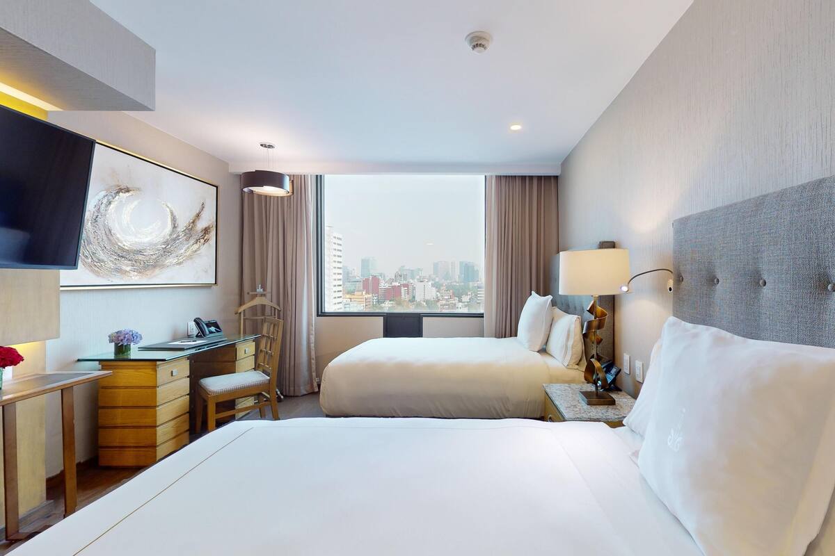 A hotel room with two beds, a desk, a chair, a TV, and a city view.