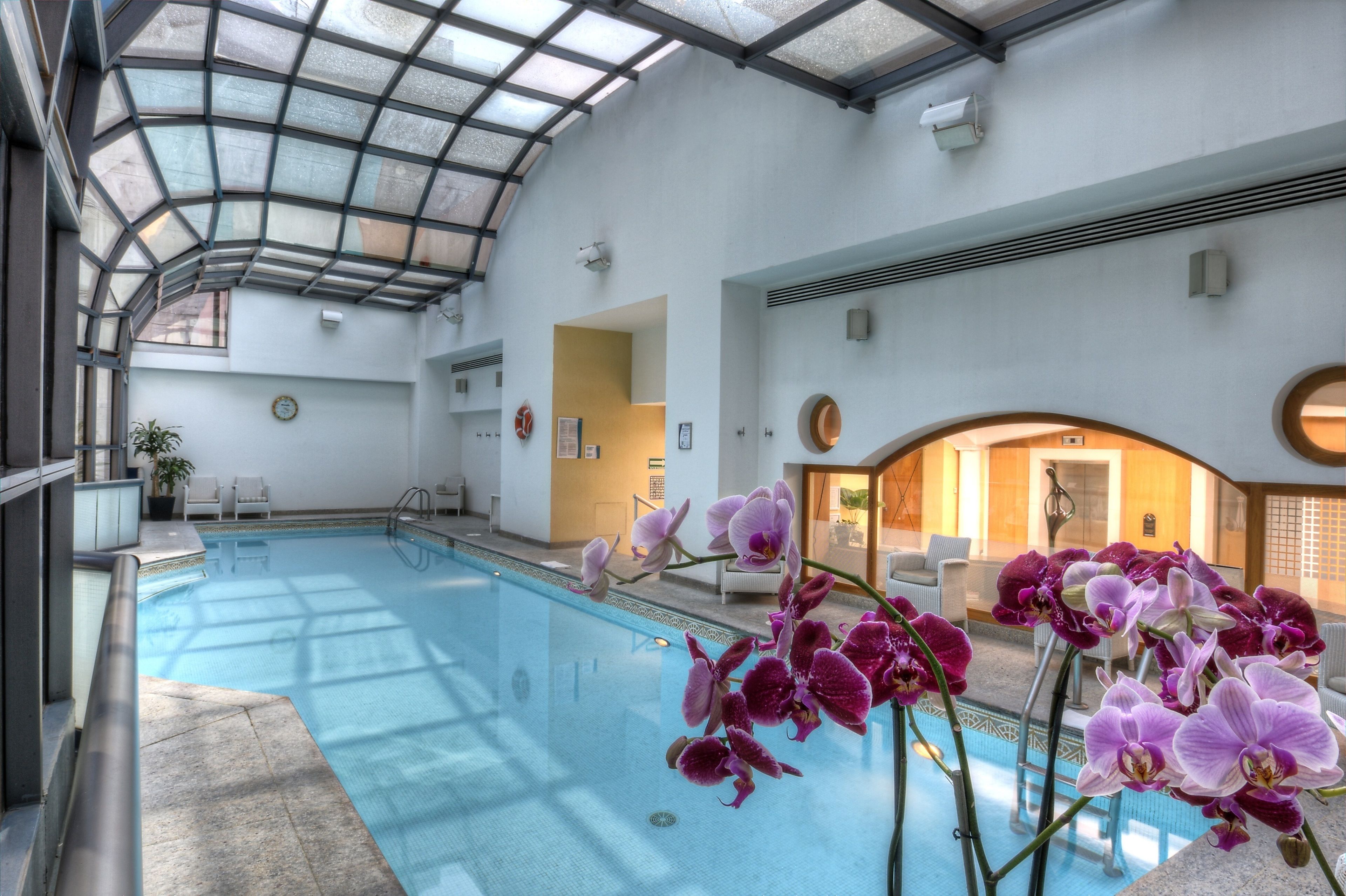 Une piscine intérieure dotée d’un toit en verre, entourée d’espaces aménagés pour s’asseoir et de plantes en pot.