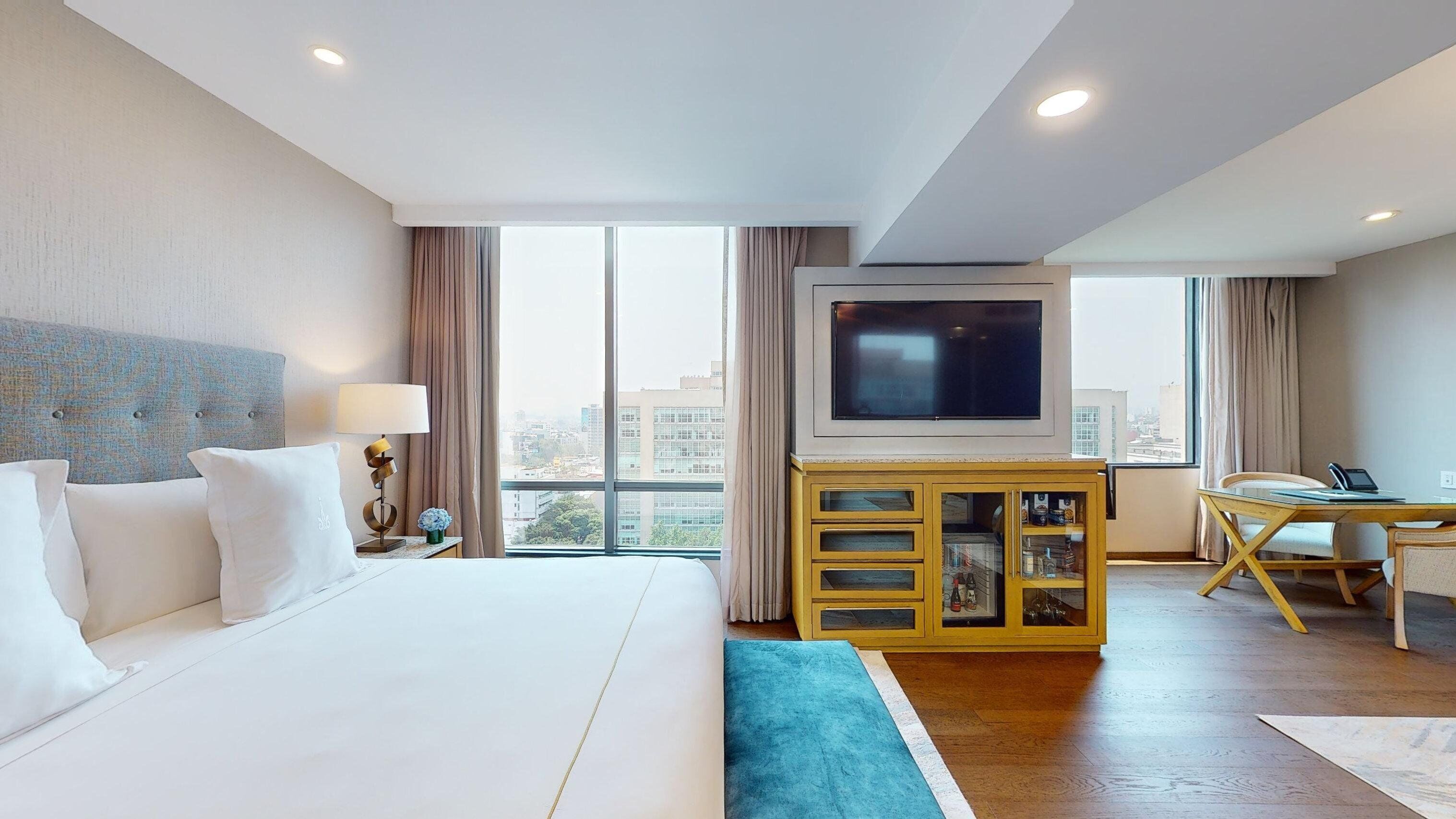 Una habitació d'hotel amb un llit gran, una televisió, un escriptori i vista a la ciutat.